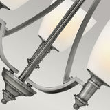 Close-up of the Truman 3 Light Chandelier - Antique Nickel, featuring brushed metal arms and etched opal glass shades. The soft lighting emits a warm glow against a neutral background.