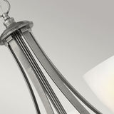A close-up of the Truman 5 Light Chandelier - Antique Nickel highlights its sleek, curved lines and central etched opal glass shade, embodying a minimalist and contemporary aesthetic against a soft gray background.