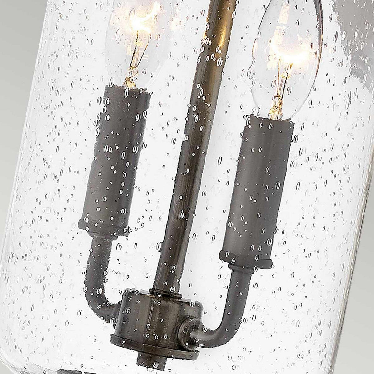 Introducing the Willoughby 2 Light Wall Lantern in Oil Rubbed Bronze, featuring a vintage-style design with two candle-shaped bulbs housed within clear seeded glass, accented by delicate air bubbles for an elegant rustic appearance. The oil-rubbed bronze finish enhances its timeless charm, making it a versatile choice for outdoor spaces.