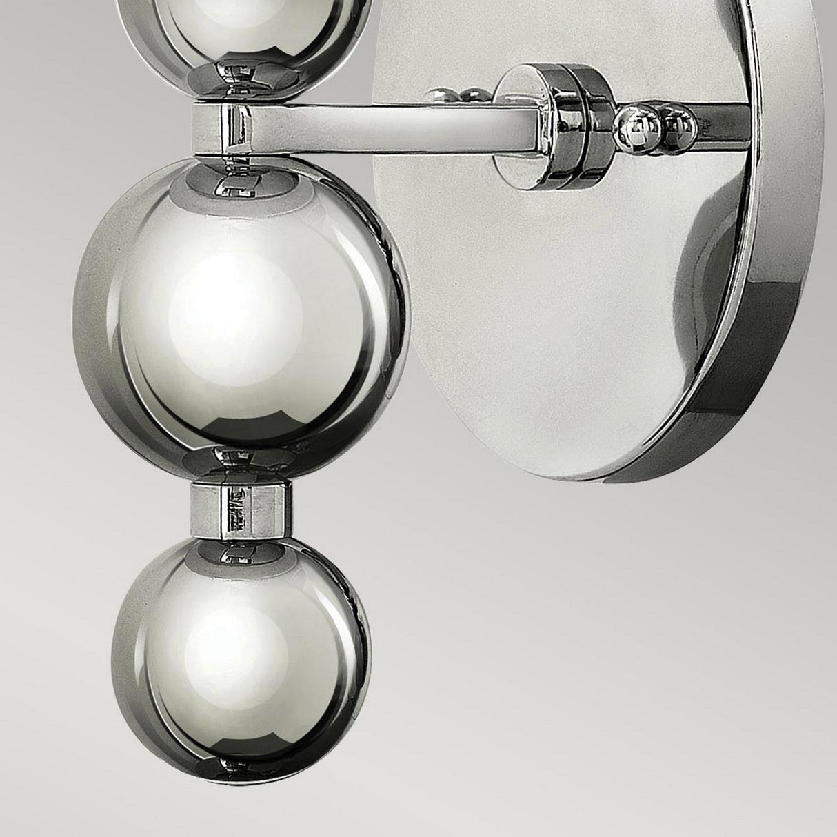 Close-up of the Zelda 1 Light Wall Light in polished nickel, featuring a circular base and two shiny spheres on a horizontal bar. The design captures a Mid-Century style, set against a neutral gray background.