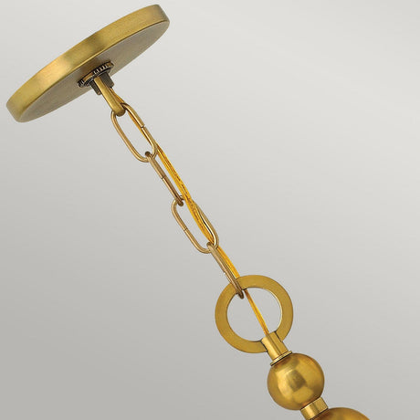 Close-up of the Zelda 5 Light Chandelier in Vintage Brass, featuring a golden chain and decorative circular elements evocative of mid-century design. This chandelier combines modern style with a smooth, shiny finish and is set against a plain gray background.