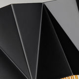 Close-up of the Zuma 3 Light Wall Light in Satin Black/Gold, showcasing its sleek geometric silhouette with sharp angular ridges and folds that form a modern, abstract pattern. The neutral gray background enhances its contemporary design with clean lines and shadows.