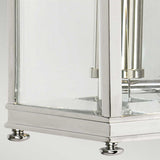 Close-up of the Holborn 1 Light Outdoor Small Wall Lantern in polished chrome, showcasing its modern rectangular glass and metal design inspired by Georgian lanterns. It stands on four small round feet, with a partially visible candle holder inside. The backdrop is an understated, neutral color.