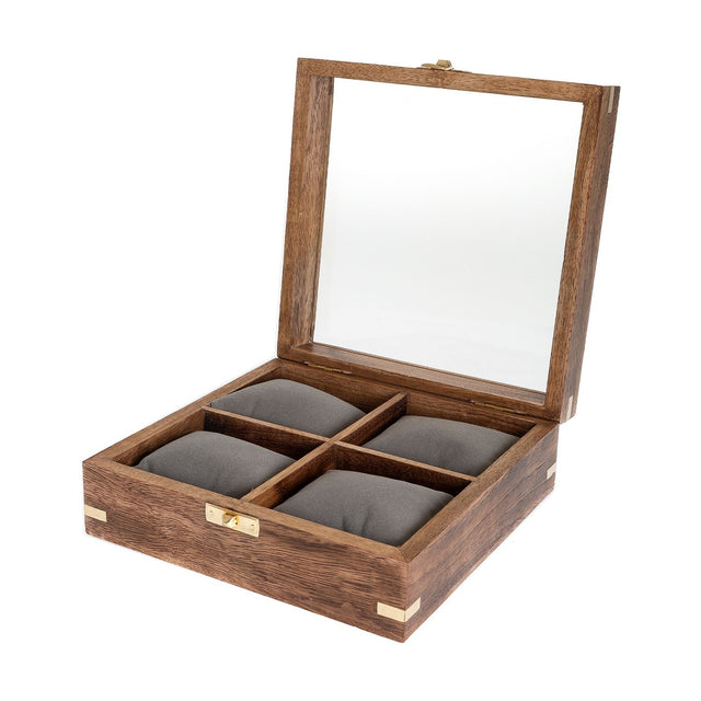 Square wooden watch box with glass-paned lid, open to show four grey cushioned compartments, brass corner accents and front clasp, on a plain white background.