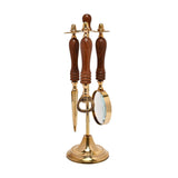 Letter opener, bottle opener, and magnifying glass with brown turned wood handles hang from a gold crossbar on a brass stand, set against a plain white background.