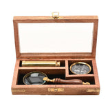 Open wooden hinged case with glass lid holding a brass telescope, compass, and magnifying glass with wooden handle, brown finish, gold fittings, white background.
