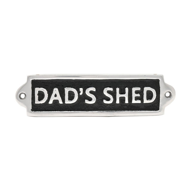 Rectangular metal wall plaque reading "DAD'S SHED" in raised silver capitals on a black panel with a silver border and two fixing holes, shown on a white background.