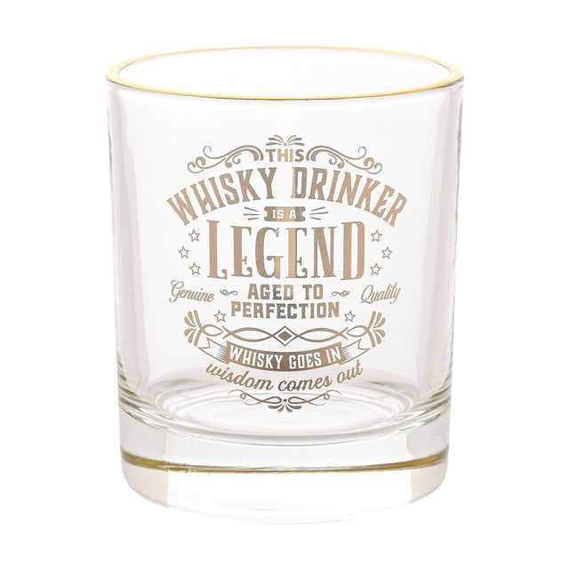 Clear glass whisky tumbler with a gold rim, featuring gold text reading "This Whisky Drinker Is A Legend, Aged To Perfection" with stars and flourishes, on a plain white background.
