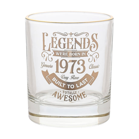 Clear glass tumbler with a gold rim, featuring gold text "Legends Were Born in 1973, Very Rare, Built to Last, Totally Awesome" with scroll detailing, on a plain white background.