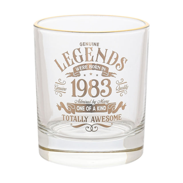 Clear glass whiskey tumbler with gold rim, printed with "Legends Were Born in 1983" vintage-style gold text and banners, shown on a plain white background.
