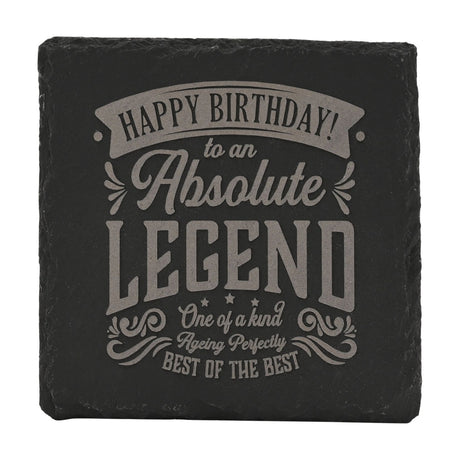 Square black slate coaster engraved with grey lettering reading "Happy Birthday to an Absolute Legend, Best of the Best," framed by scrolled flourishes on a white background.