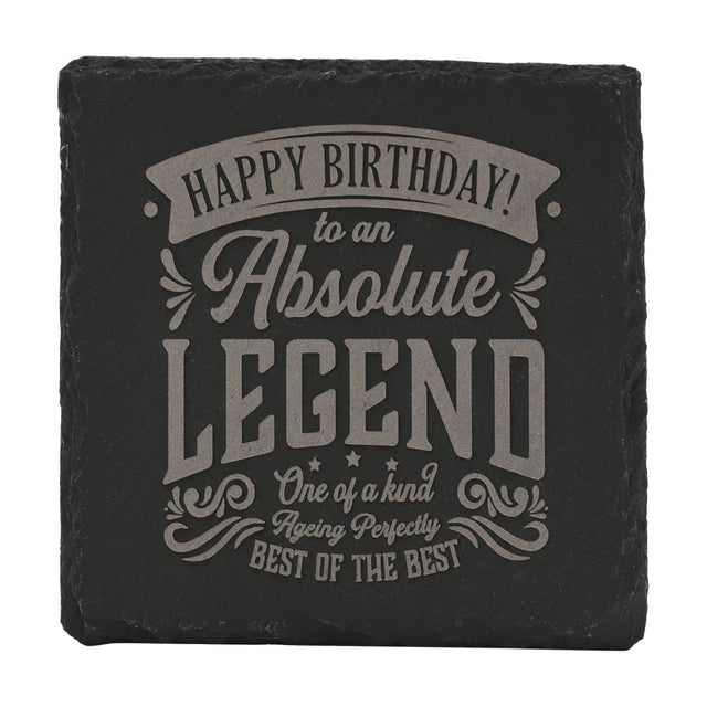 Square black slate coaster engraved with grey lettering reading "Happy Birthday to an Absolute Legend, Best of the Best," framed by scrolled flourishes on a white background.