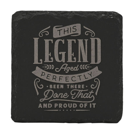 Square black slate coaster engraved with grey lettering reading This Legend Aged Perfectly, Been There, Done That and Proud of It, framed by ribbon banners and wheat sprigs.