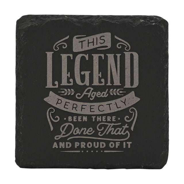 Square black slate coaster engraved with grey lettering reading This Legend Aged Perfectly, Been There, Done That and Proud of It, framed by ribbon banners and wheat sprigs.