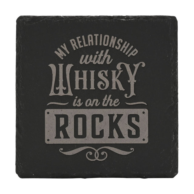 Square black slate coaster engraved with "My Relationship with Whisky Is on the Rocks" in pale grey lettering, ROCKS set in a plaque panel, shown on a white background.