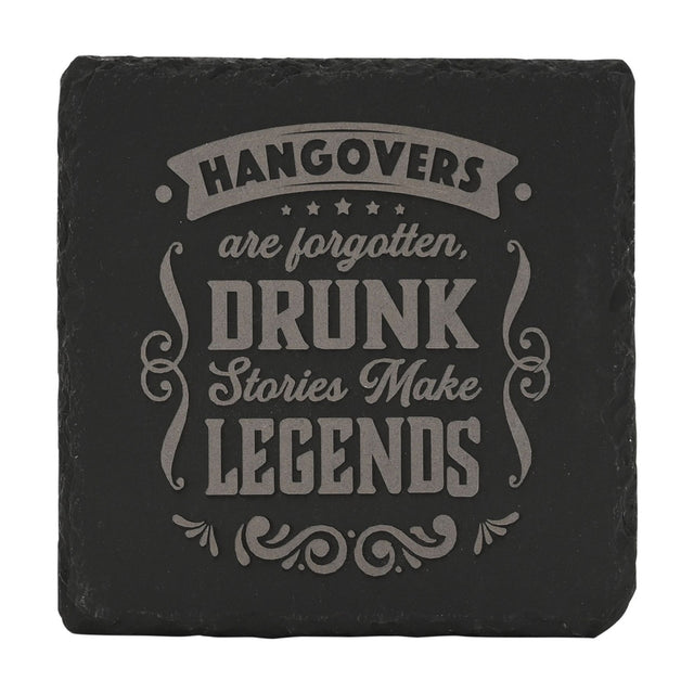 Square black slate coaster with raw edges, engraved in grey with "Hangovers are forgotten, drunk stories make legends" within a banner, stars, and scrollwork design, on a plain white background.