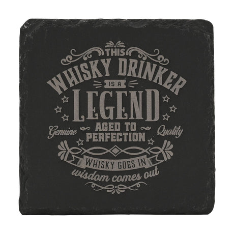 Black square slate coaster engraved in grey with "This Whisky Drinker Is a Legend, Aged to Perfection, Whisky Goes In Wisdom Comes Out" text and decorative scrolls, stars, on a white background.