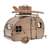 Teardrop caravan figurine in gold metal with ribbed corrugated panels, panelled door, framed windows, and a roof rack holding a surfboard and suitcase, shown on a plain white background.