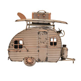 Teardrop Caravan Ornament metal figurine in gold with aged edges, corrugated panels, framed windows, and a roof rack holding a surfboard and suitcase, shown on a plain white background.