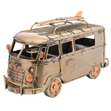Weathered bronze metal campervan figurine with roof-rack surfboard, mesh grille, round headlamps, copper-edged window frames and visible steering wheel, shown on a plain white background.