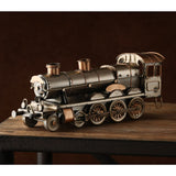 Steam Train Metal Ornament Figurine with copper trim, antique bronze locomotive with riveted boiler, twin stacks and spoked wheels, displayed on a wooden table against a dark background.