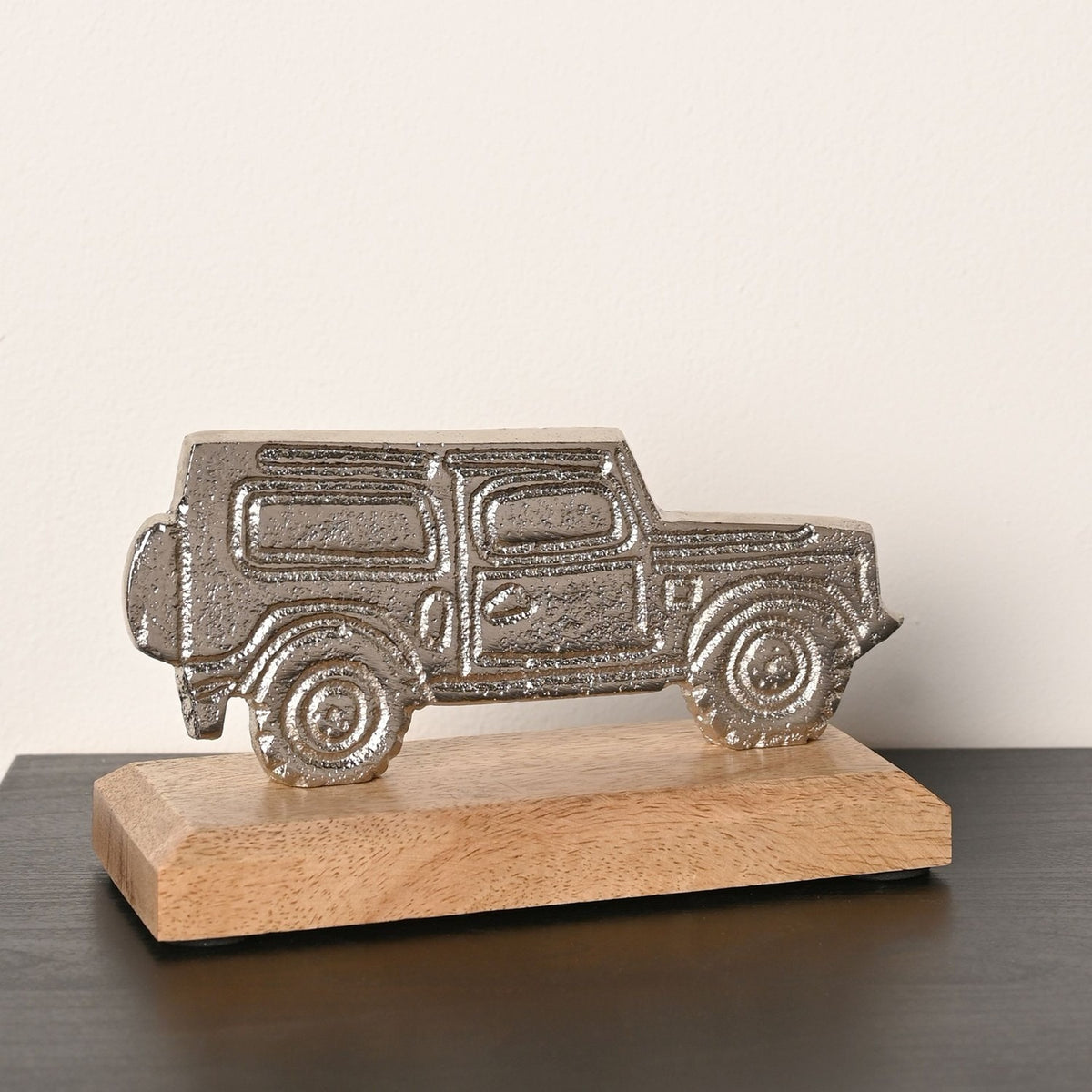4X4 Vehicle Metal Figurine with Base in silver, a flat textured silhouette on a natural wood base, shown on a dark surface against a plain light background.