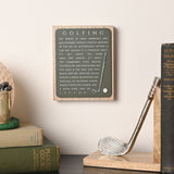 Golf Wooden Plaque with Club and Ball in green and natural wood, featuring white "Golfing" lettering and a raised club and ball design, displayed on a shelf with books and bookends.