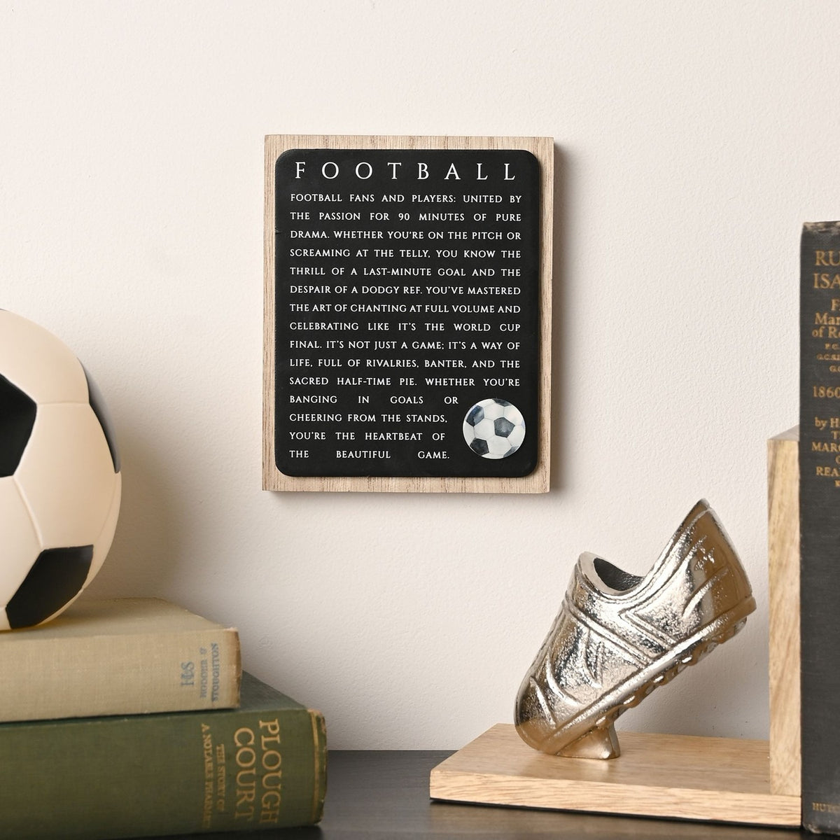 Football Wooden Plaque with Ball Motif in black and natural wood, hung on a wall beside books, a football and a boot-shaped bookend.