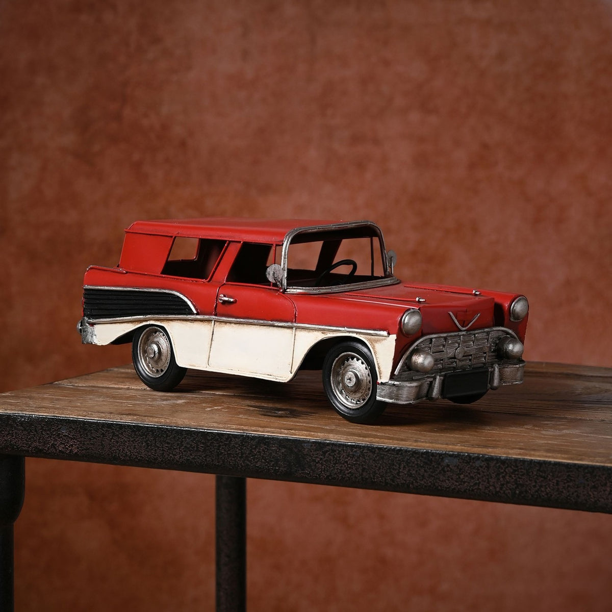Retro Estate Car Metal Figurine with Tail Fins in red with cream lower panels, silver trim, bumpers and hubcaps, shown on a wooden table against a rust-toned background.