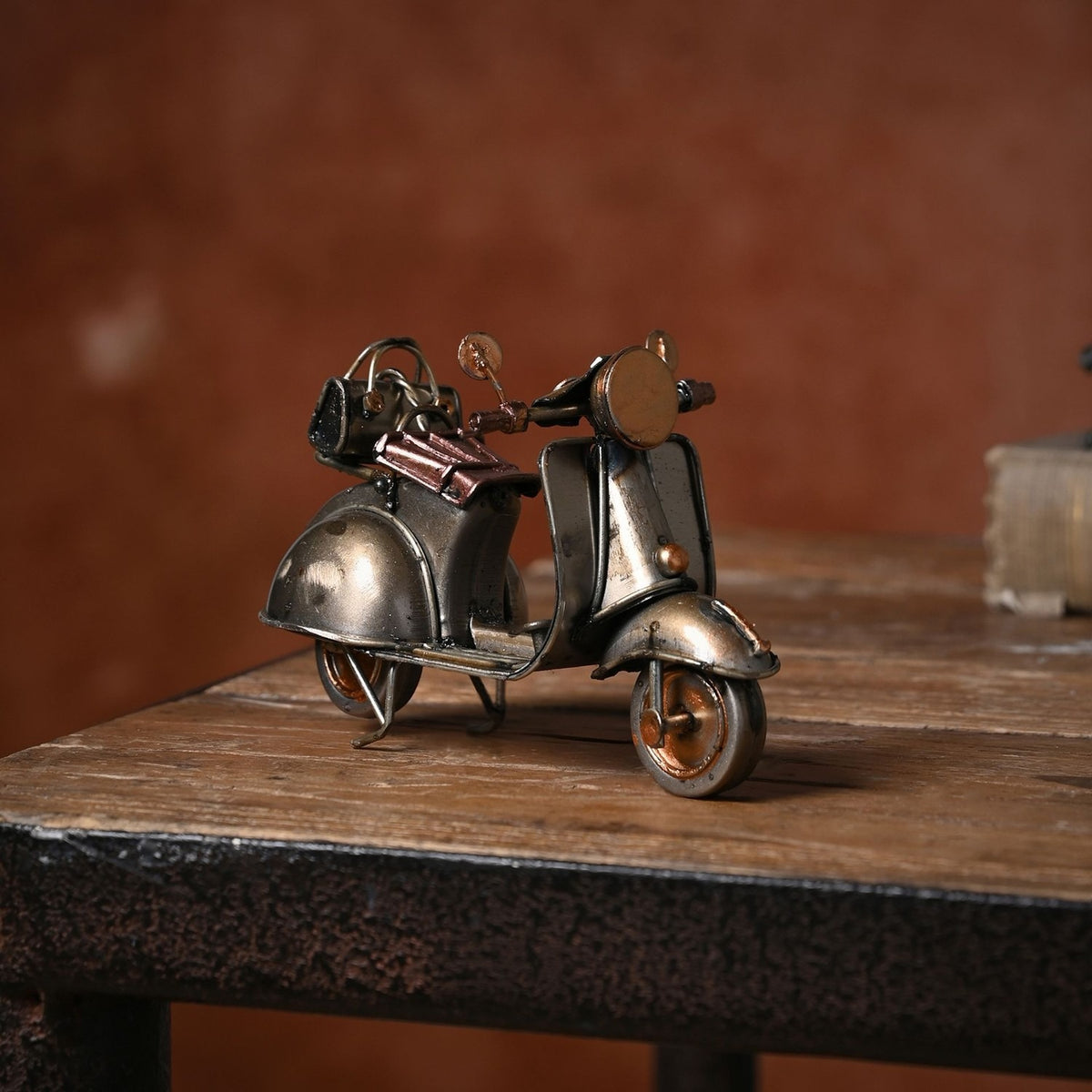 Retro Scooter Metal Ornament Figurine in antique bronze and copper, with round headlamp, twin mirrors and copper seat, displayed on a wooden table against a red wall.