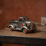 Vintage Pickup Truck Metal Ornament Figurine in silver with copper-tone grille, headlamps and hubcaps, shown on a wooden surface against a dark red wall.