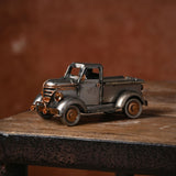 Vintage Pickup Truck Metal Ornament Figurine in silver with copper-tone grille, headlamps and hubcaps, shown on a wooden surface against a rust-toned background.
