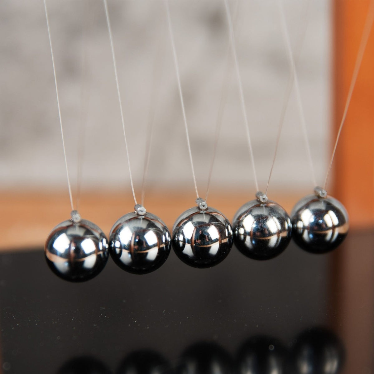 Close-up of a wooden Newton's cradle with black base, showing five silver metal balls suspended on clear threads from a brown frame with matt finish.