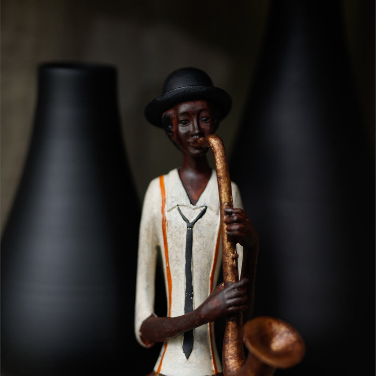 Hill Interiors saxophonist figurine in resin, wearing a bowler hat and white jacket with tie, playing a bronze-toned sax beside dark vases.