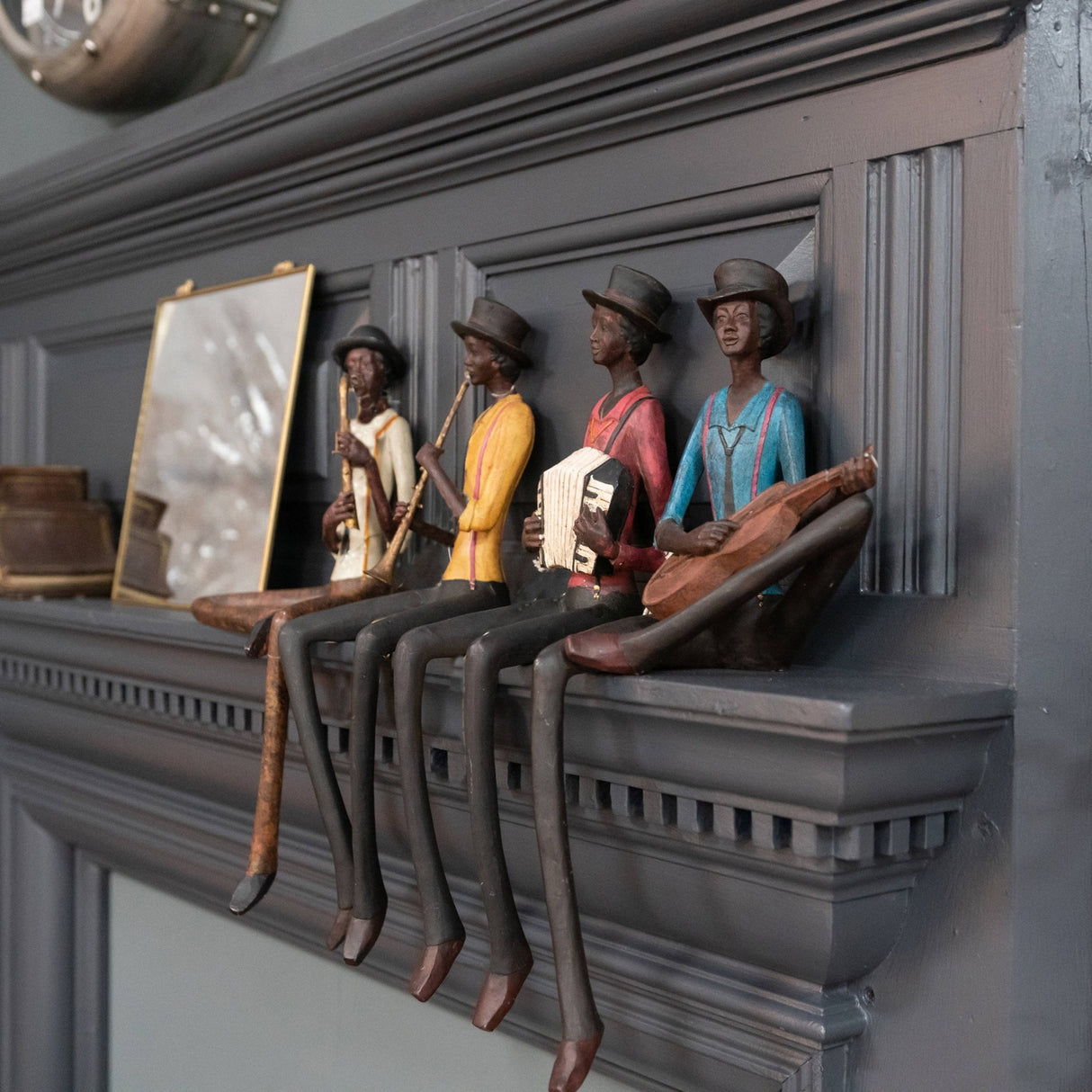 Hill Interiors Sitting Musician Figurines lined up on a dark grey mantelpiece, seated players in top hats holding a trumpet, clarinet, accordion and guitar.