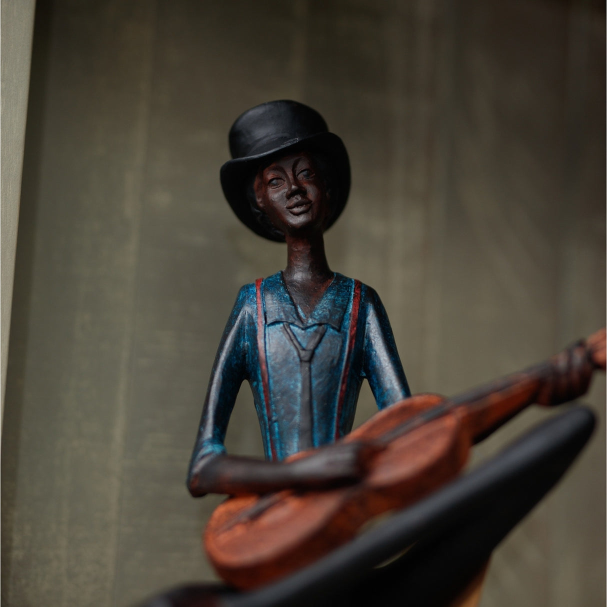 Hill Interiors Sitting Musician Figurine in brown resin, wearing a black bowler hat and blue jacket, holding a stringed instrument against a neutral backdrop.