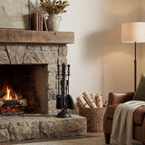 Hill Interiors Black Fireside Companion Set with poker, brush, shovel and tongs on an upright stand beside a stone fireplace and log basket.
