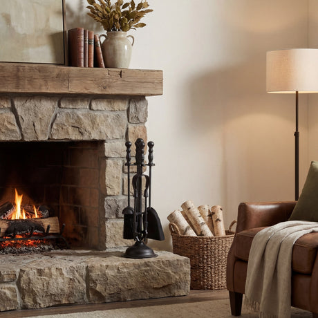 Hill Interiors Ball-Topped Fireside Companion Set in black metal with poker, brush, shovel and tongs on an upright stand beside a stone fireplace.