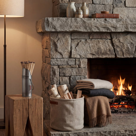 Hill Interiors Antique Pewter Match Holder in silver filled with long matches, set on a wood block beside a stone fireplace with logs and blankets.