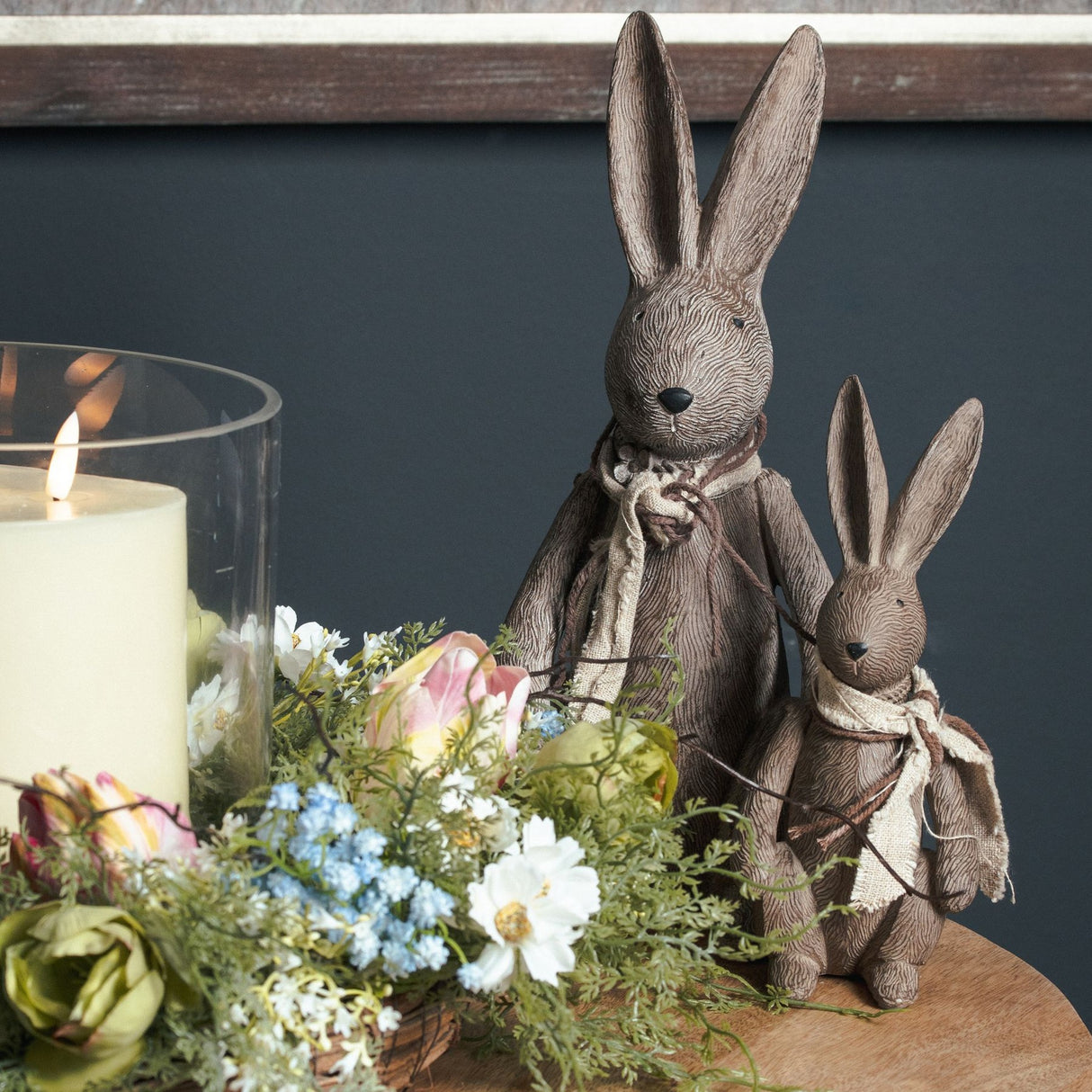 Hill Interiors Large Winter Bunny Rabbit Figurine in brown resin, shown with a smaller bunny beside a candle and floral arrangement on a wooden table.