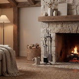 Hill Interiors Hand Turned Loop Top Companion Set in silver metal, with poker, brush, shovel and tongs on a looped stand beside a rustic stone fireplace.