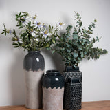 Hill Interiors Medium Ceramic Vase in white with a two-tone glazed and textured finish, holding white flowers beside two darker ceramic vessels with eucalyptus.
