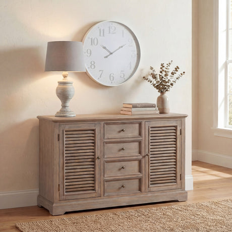 Hill Interiors Wooden Table Lamp in beige with a turned solid wood base and tapered linen shade, lit on a wooden sideboard beneath a large wall clock.