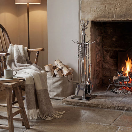 Hill Interiors hand turned stag companion set in polished nickel beside a stone fireplace, with poker, brush, shovel and tongs on a freestanding stand.