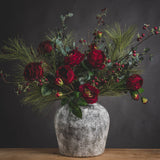 Hill Interiors Aged Stone Ceramic Vase in beige holding a festive arrangement of red ranunculus, eucalyptus, pine needles and berry stems.
