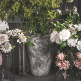 Hill Interiors tall ceramic floor vase in aged stone beige finish, holding foliage and white blooms among dahlias and pink roses in a florist display.