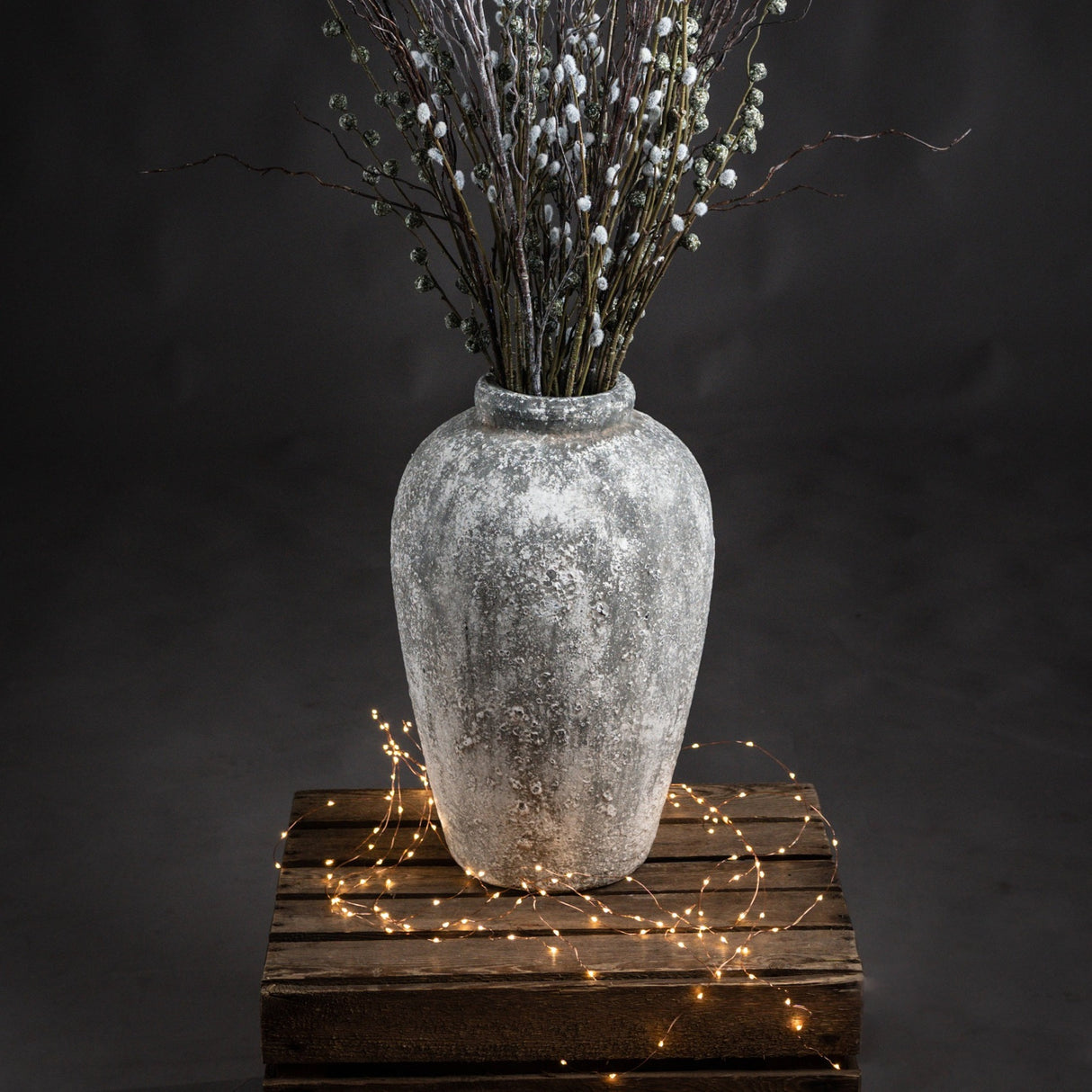 Tall Hill Interiors ceramic vase in aged stone beige finish, holding frosted berry branches, displayed on a rustic wooden crate with fairy lights.