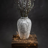 Tall Hill Interiors ceramic vase in aged stone beige finish, holding frosted berry branches, displayed on a rustic wooden crate with fairy lights.