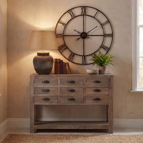 Hill Interiors Aged Stone Ceramic Table Lamp in beige with tapered linen shade, styled on a rustic wooden console with books, plant and large clock.