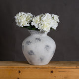Hill Interiors Large Antique White Ceramic Vase with distressed matte finish and urn-shaped body, holding white hydrangeas on a wooden surface.